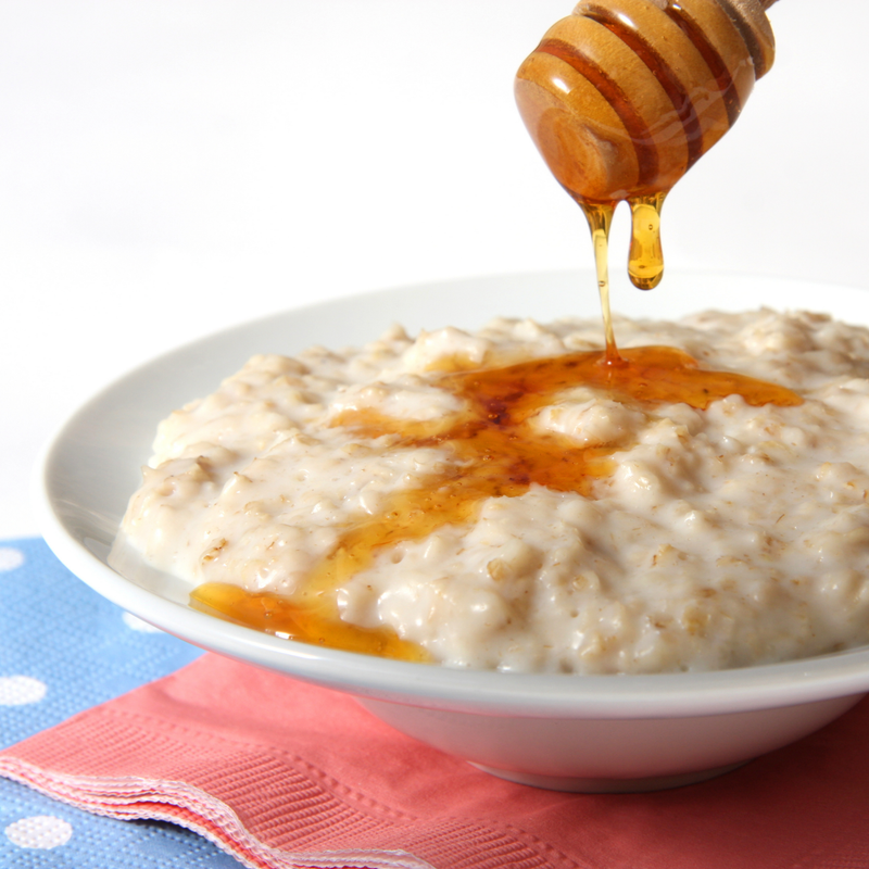 Bowl of oatmeal with honey being drizzled over it on a white background