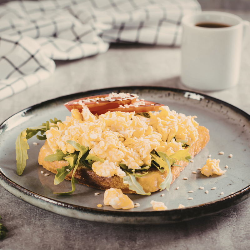 Scrambled eggs on toast with arugula on a gray plate, coffee in the background